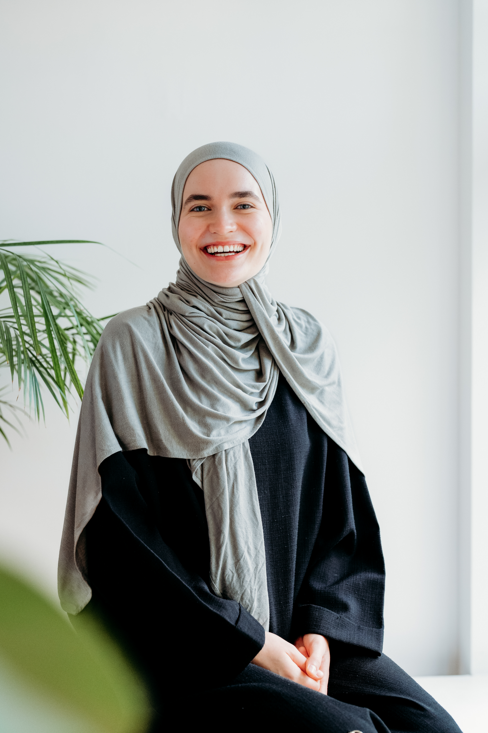 A smiling woman wearing a grey hijab and a black top.